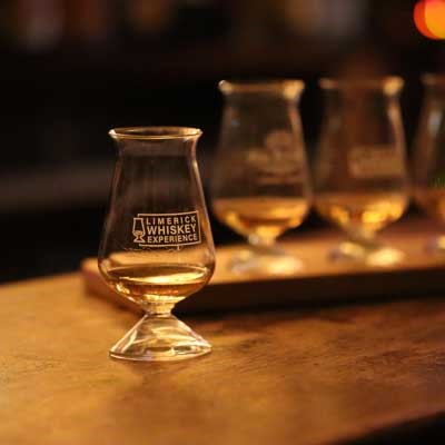 A Whiskey glass on a bar counter with three glasses in the background