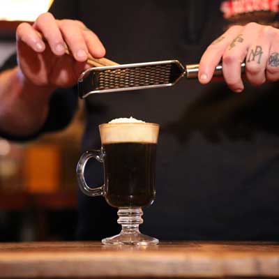 A perfect prepared Irish coffee on a counter with cinnamon being grated on the cream top